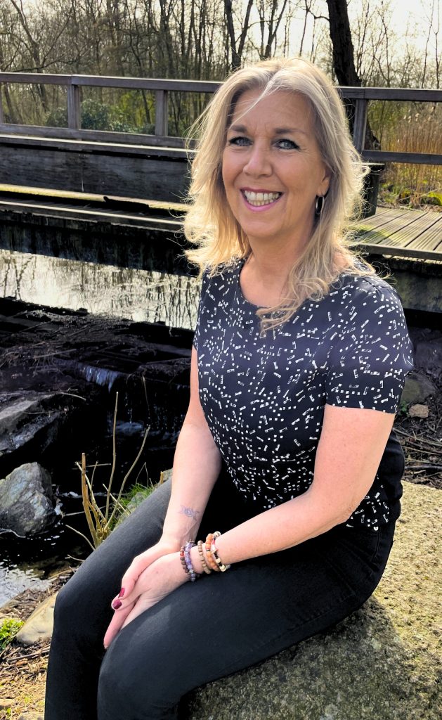 Marianne Snijder van Whichway loopbaancoaching zit lachend op een rots bij het water van de Kralingse plan in Rotterdam.